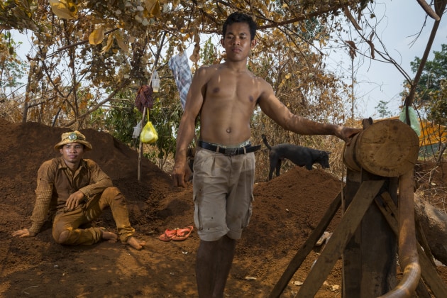 Two men rest next to the hand-powered winch used to bring up dirt from their hand-dug gem mine in rural Rattanakiri, Cambodia, 2016. © Jerry Redfern.