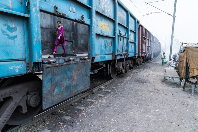 © Ashley Crowther. Young girl scavenges for leftover coal on a coal train for cooking fuel in Central India. These coal trains deliver vast amount of domestic and imported coal to factories and power plants across the Indian sub-continent. The coal, when burnt in either a kitchen or a factory, releases vast amounts of carbon dioxide contributing to the global impacts of climate change.